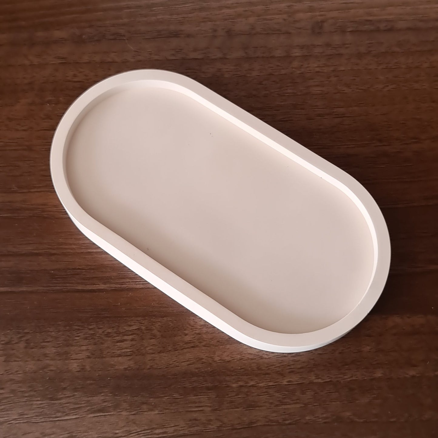 Beige oval trinket tray on a wooden background.