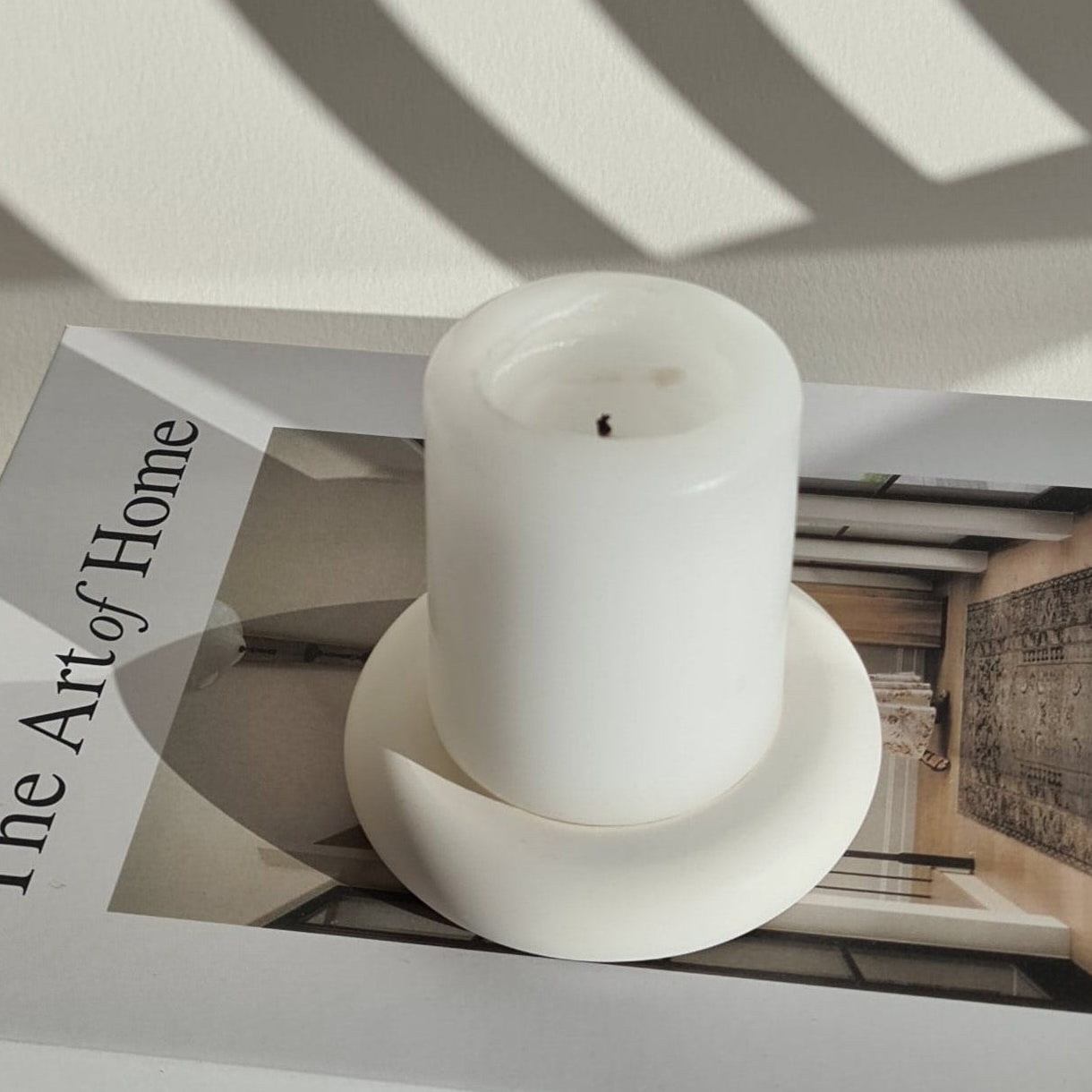 White bukhoor burner holding a candle on a book titled 'The Art of Home' with a neutral background