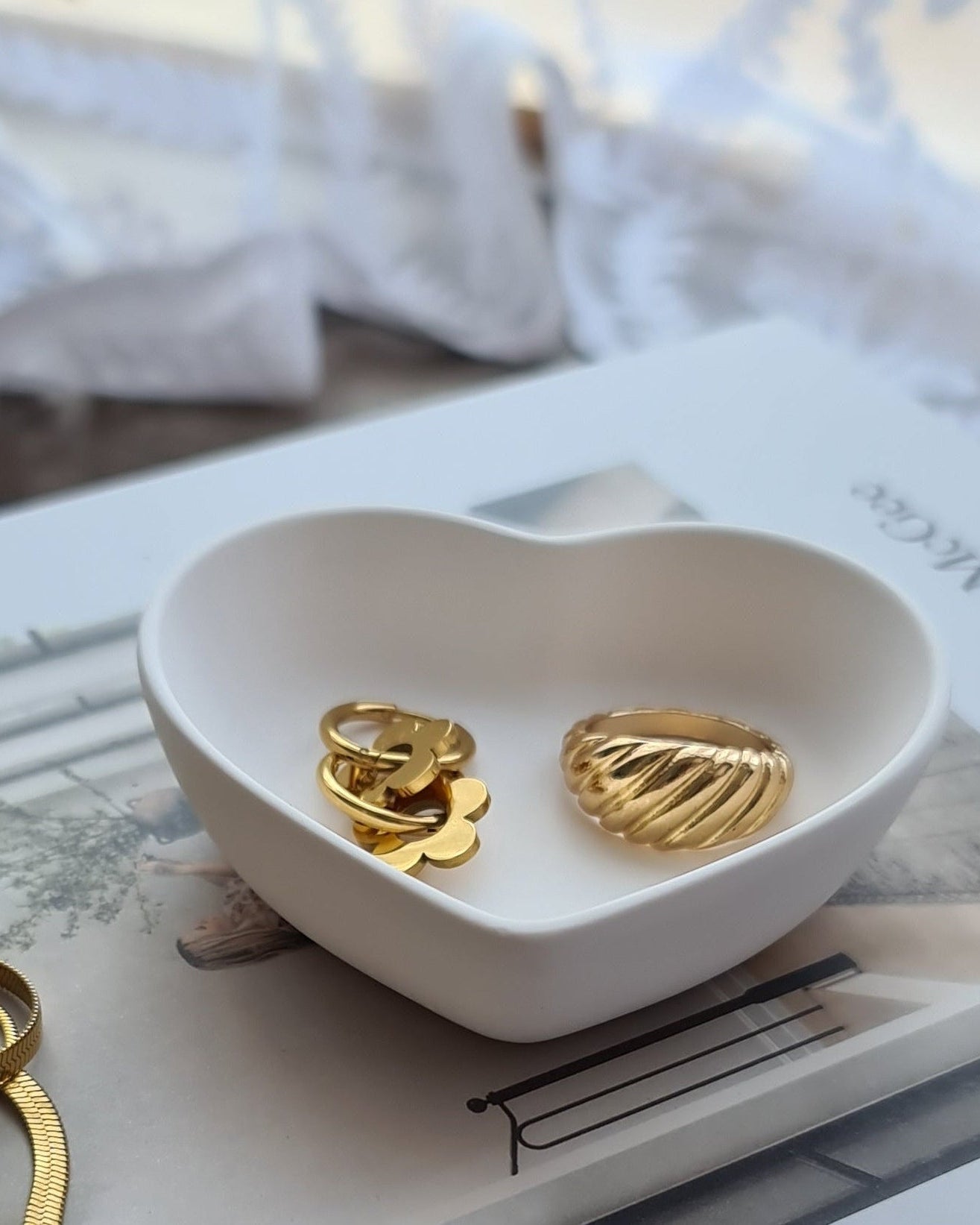 Heart-shaped white dish with gold earrings on a textured surface