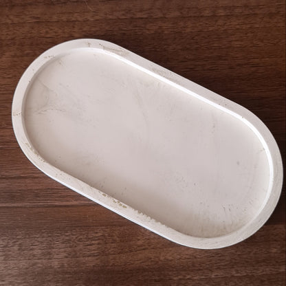Natural white oval trinket tray with light gold metal streaks on wood surface.