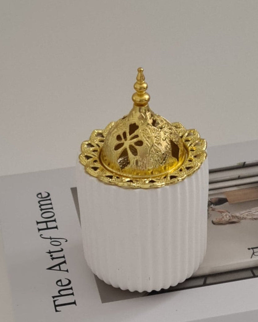 Decorative white bukhoor burner with golden dome on a magazine