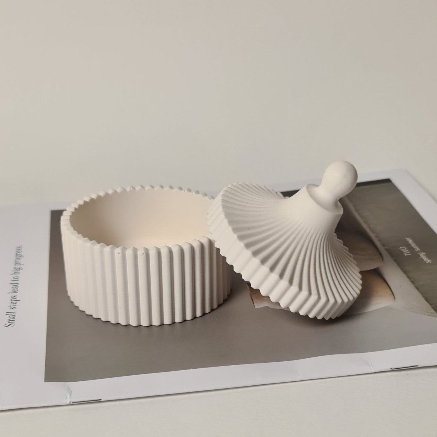 White ceramic jar and lid on a magazine called Aurora on a light gray background.