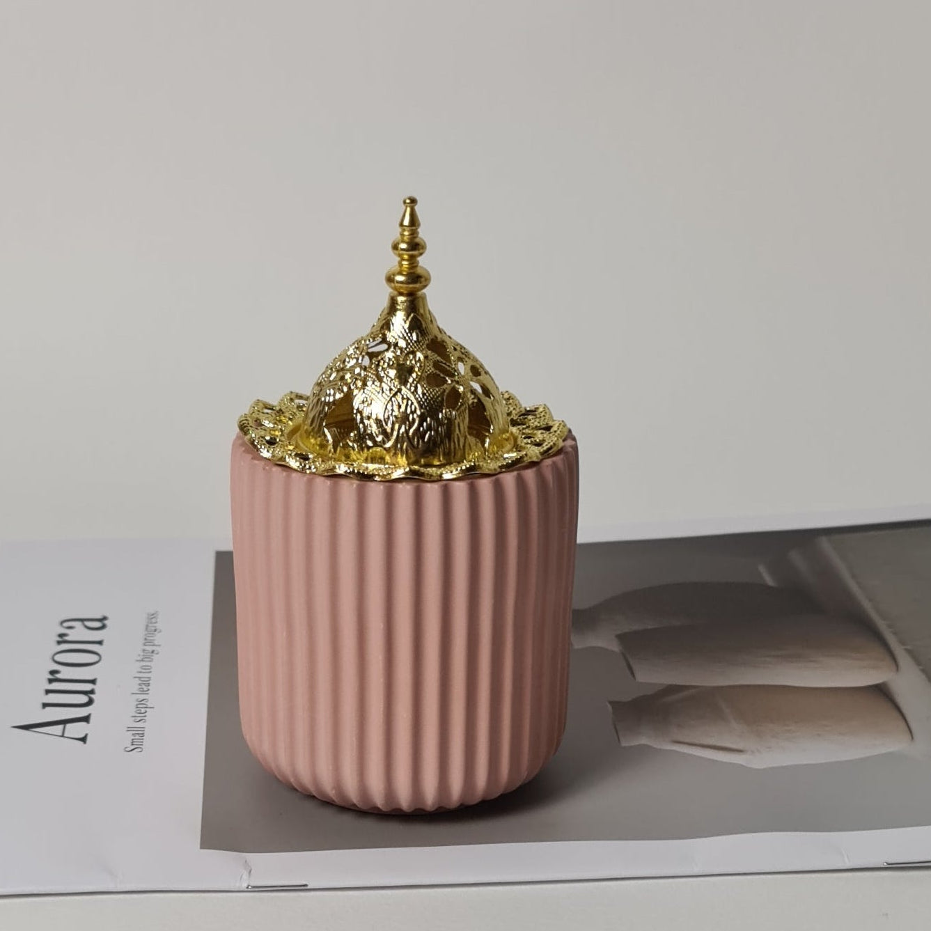 Dusty rose bukhoor burner with gold filigree dome on a magazine