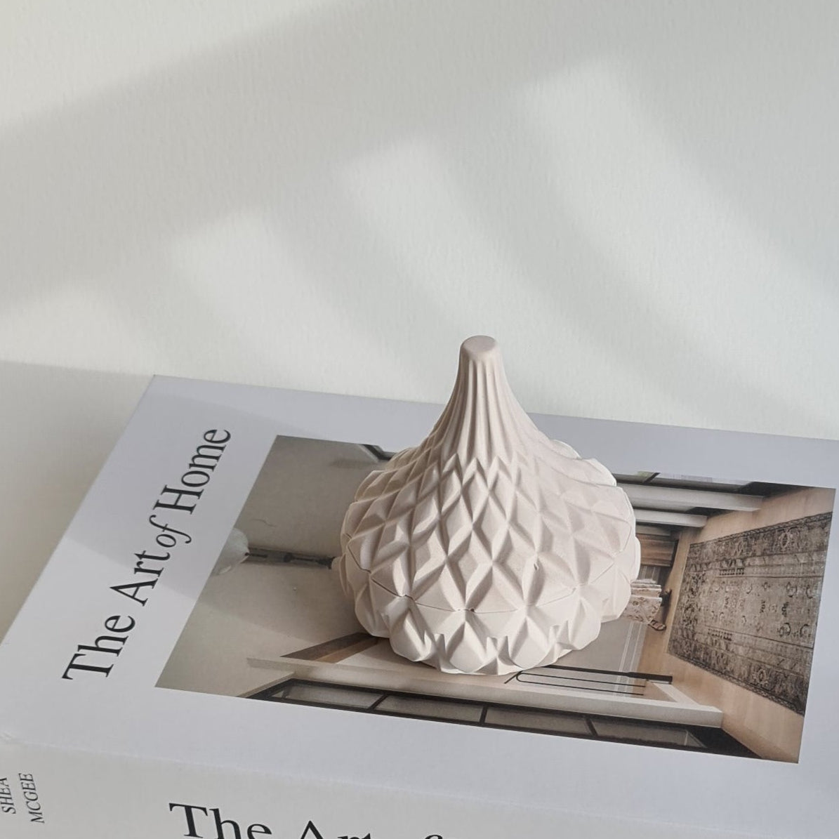Decorative jar with a book titled 'The Art of Home' on a white wall.