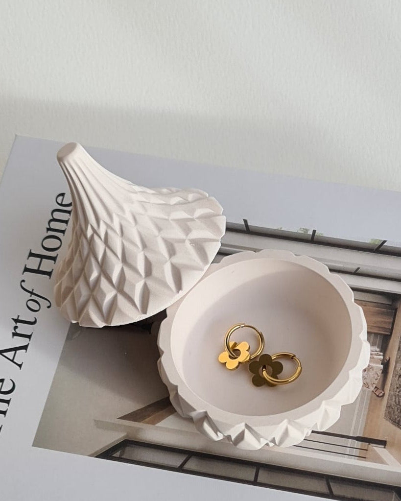 Decorative white bowl with gold earrings on a magazine titled 'The Art of Home'.