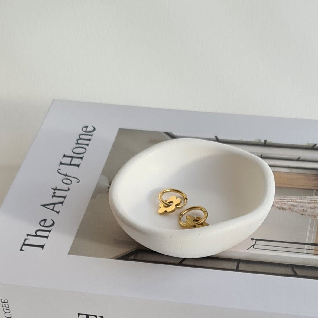 White dish with gold earrings on a book titled 'The Art of Home'.