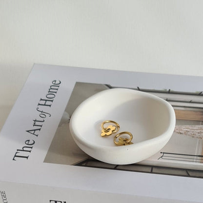 White dish with gold earrings on a book titled 'The Art of Home'.