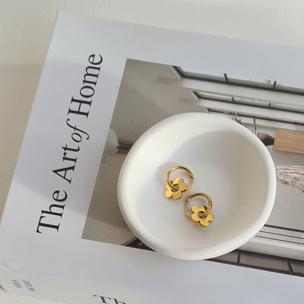 Small white dish with gold earrings on a box labeled 'The Art of Home'.