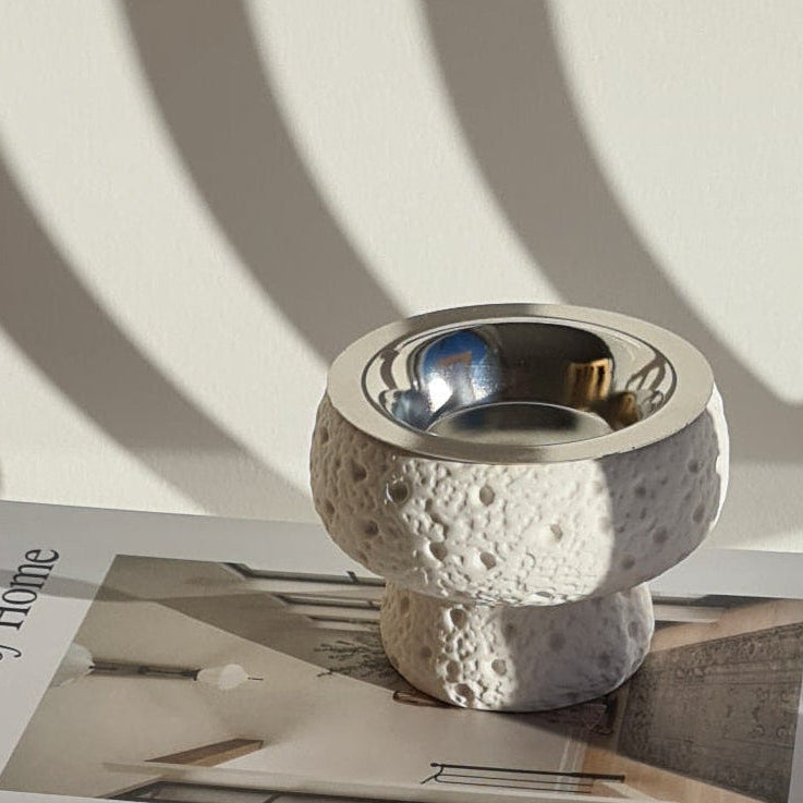 Stone-like textured bukhoor burner on book titled 'The Art of Home' on white surface in natural light