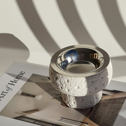 White bukhoor burner on a book titled 'The Art of Home' with sunlight casting shadows.