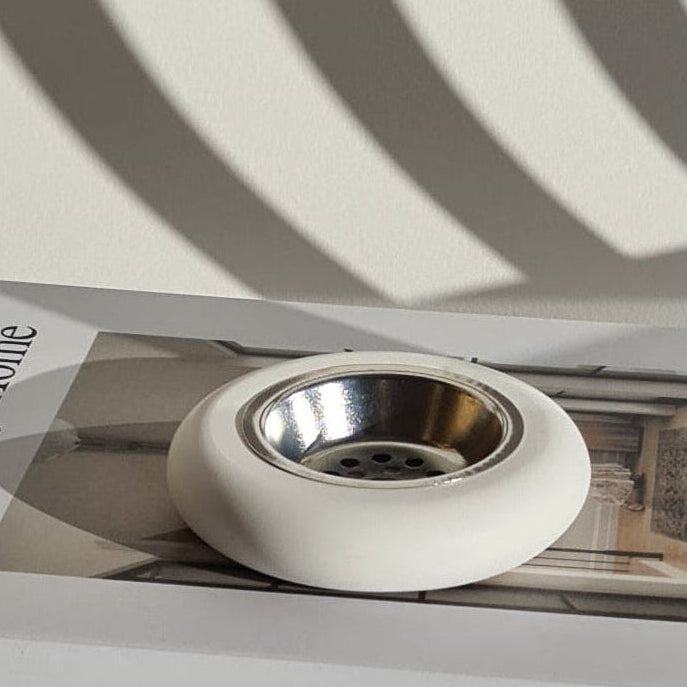 White and modern Layali bukhoor burner on top of a book titled 'The Art of Home' with concentric circle shadows.