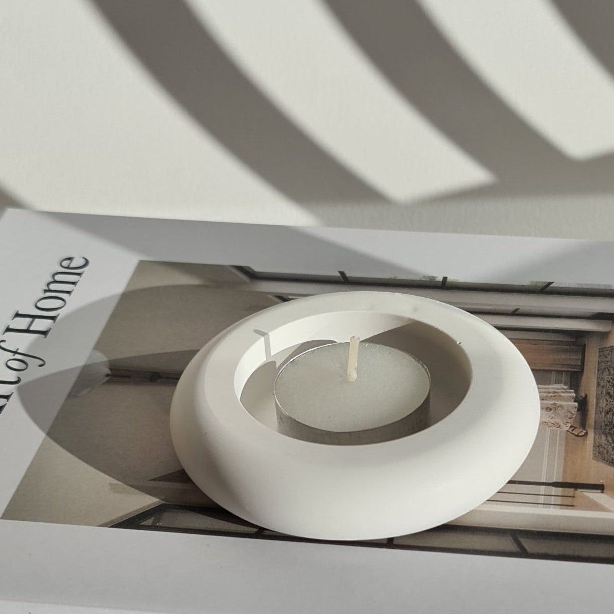 A tealight in a decorative holder on top of a book titled 'The Art of Home'.