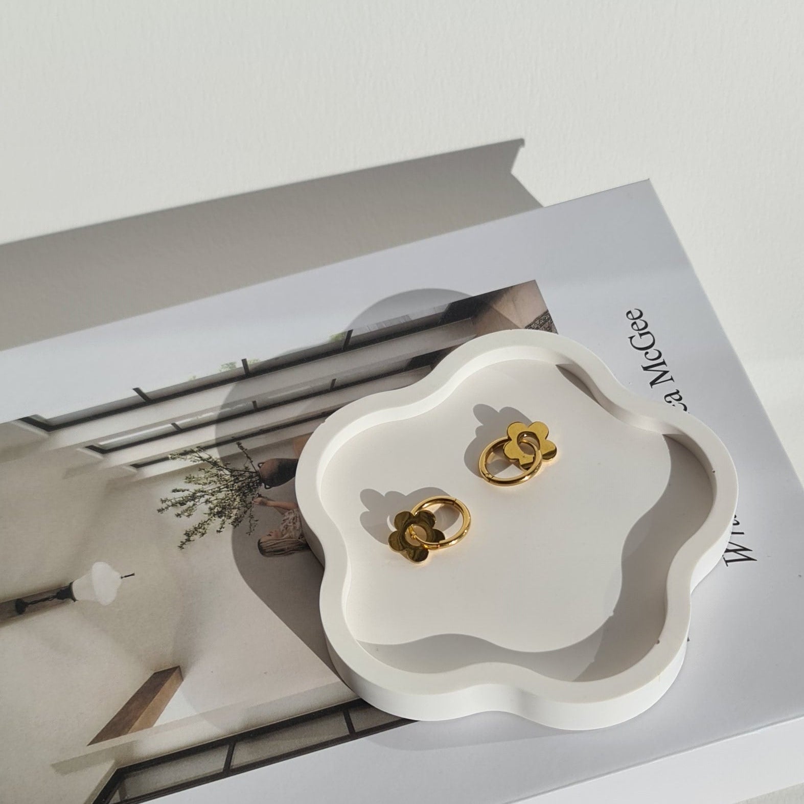 Gold earrings on a white flower-shaped dish with a magazine in the background