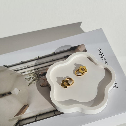 Gold earrings on a white flower-shaped dish with a magazine in the background