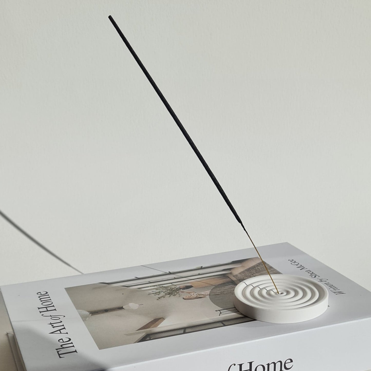 Incense holder on 'The Art of Home' book on a white surface.