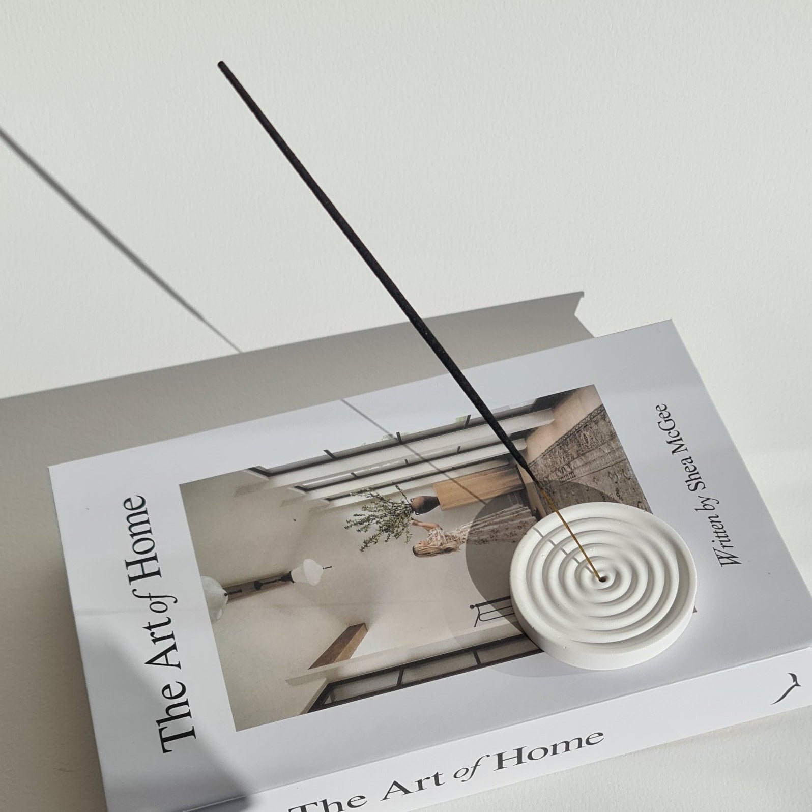 Incense stick holder on book titled 'The Art of Home' on a white surface