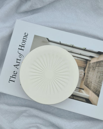 Natural white circular jar on a book titled 'The Art of Home' on a textured surface.