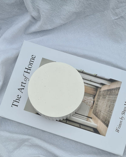 White Lina jar on a book titled 'The Art of Home' with white linen sheet in background