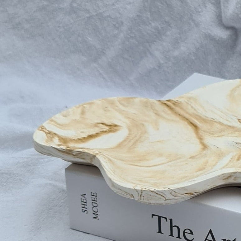 Marbled Dune tray and petal dish on a book. on a white linen sheet.