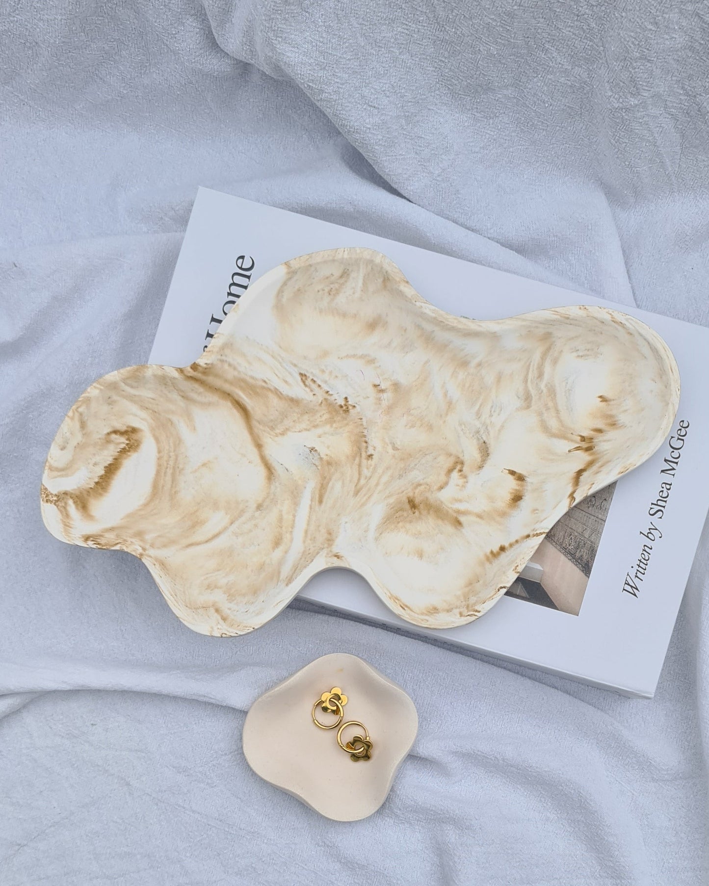Dune tray and petal dish holding earrings, on a book. on a white linen sheet