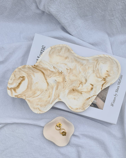 Dune tray and petal dish holding earrings, on a book. on a white linen sheet