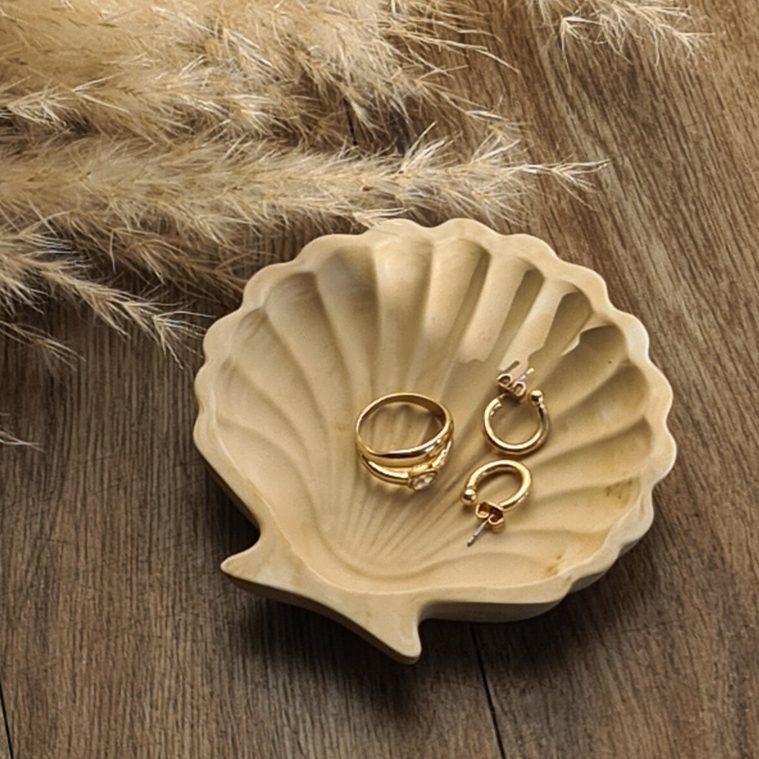 Shell with gold jewellery on a wooden surface with pampas