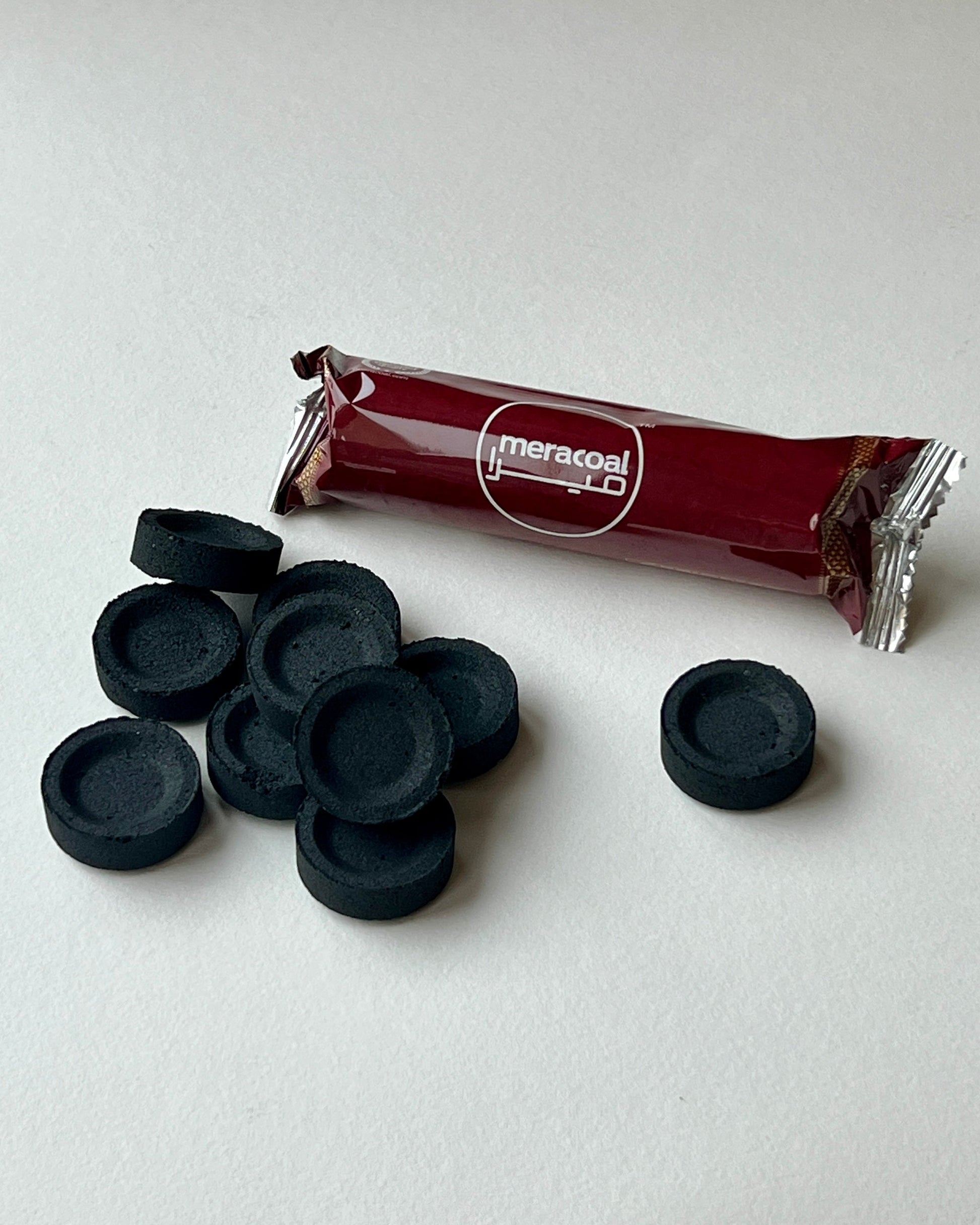 Black Instant-Light Charcoal discs and a red-wrapped pack of charcoal discs on a white surface