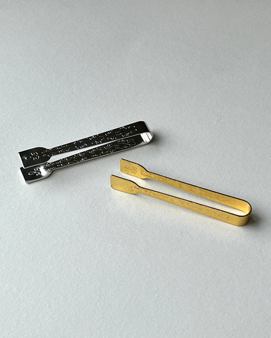 Two metal tongs, one gold and one silver, on a light gray background