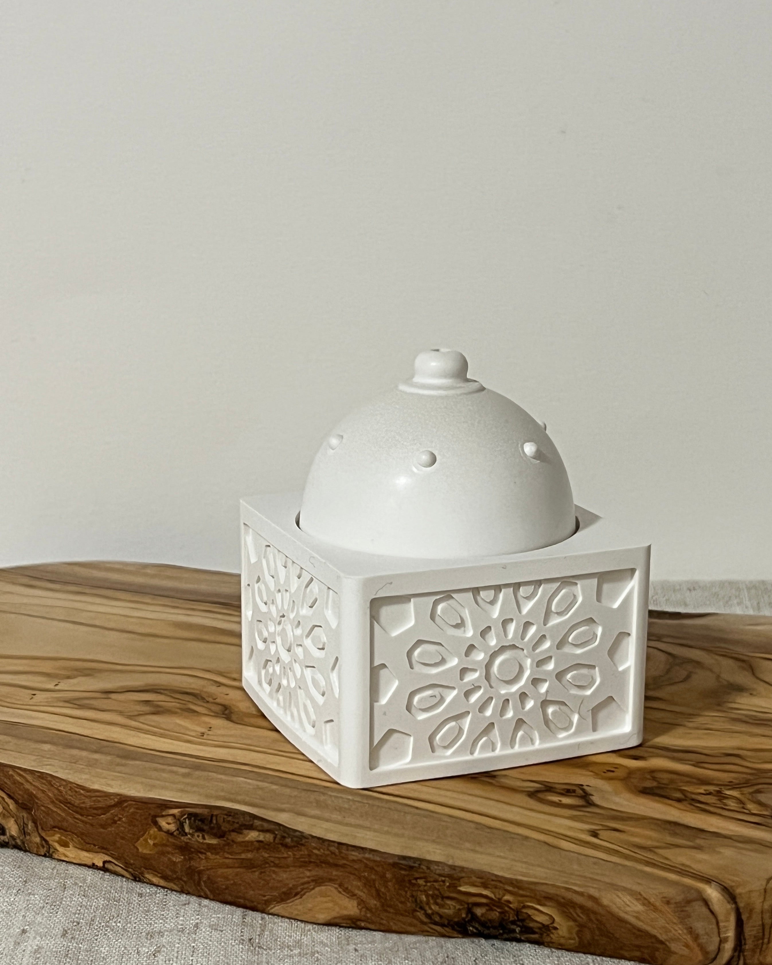 square bukhoor burner with dome on a wooden board with a neutral background