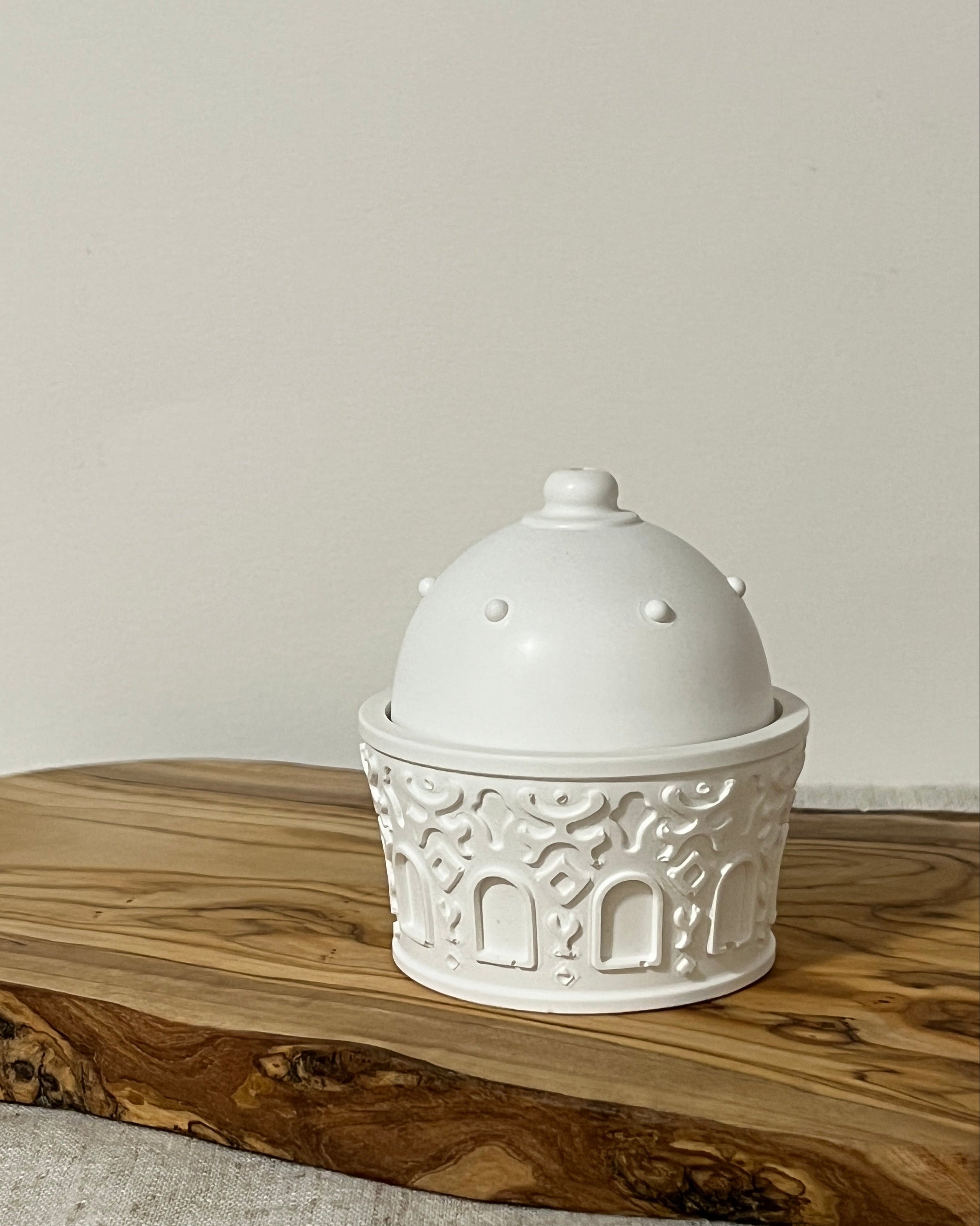 a textured bukhoor burner with a dome lid on a wooden board