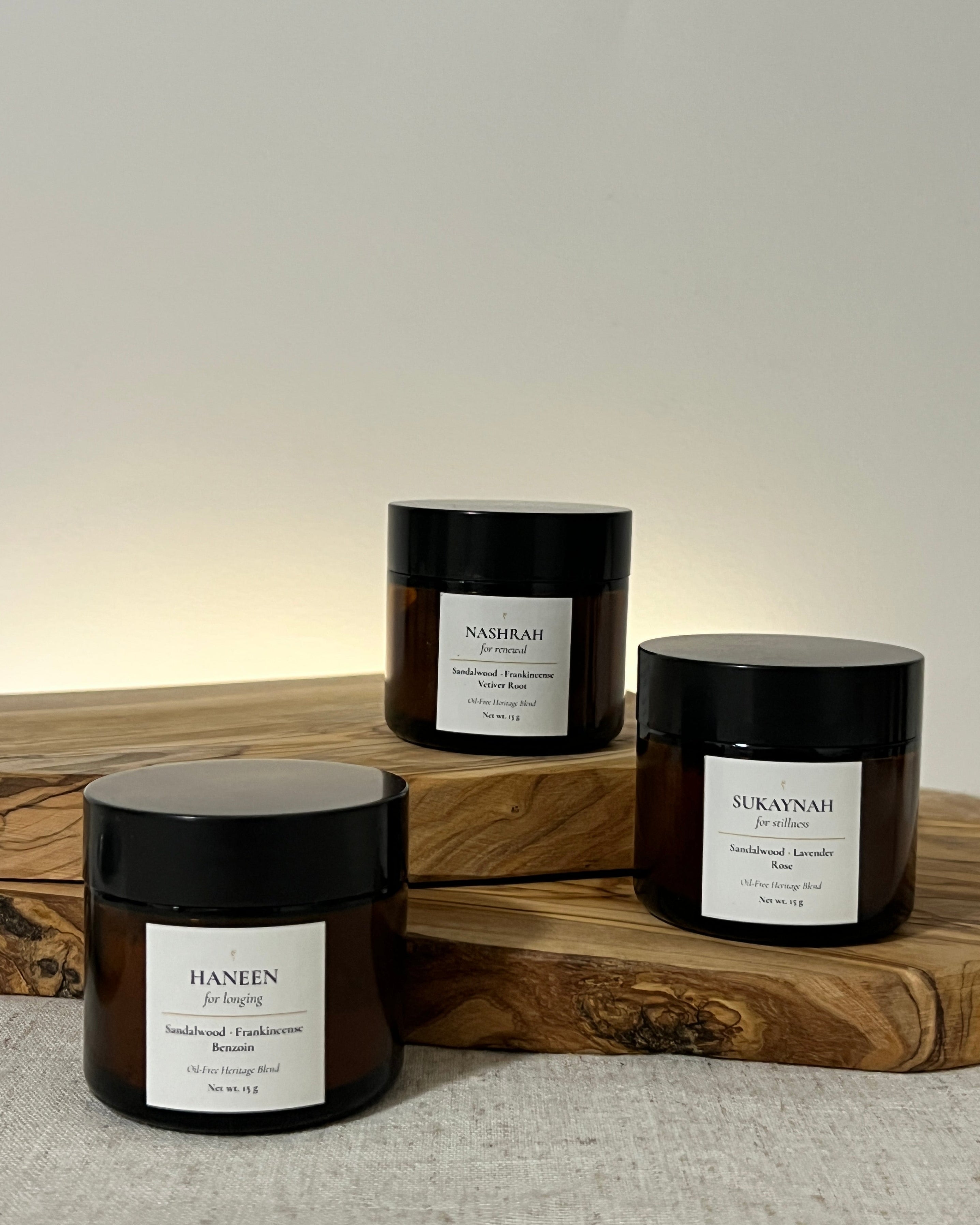 Three amber jars filled with oil-free bukhoor, on wooden board, and neutral background