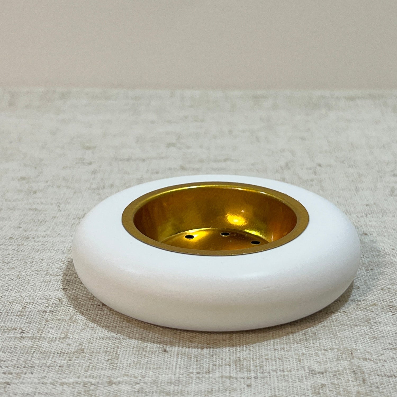 Round white low bukhoor burner with old gold/brass plate on a textured beige background