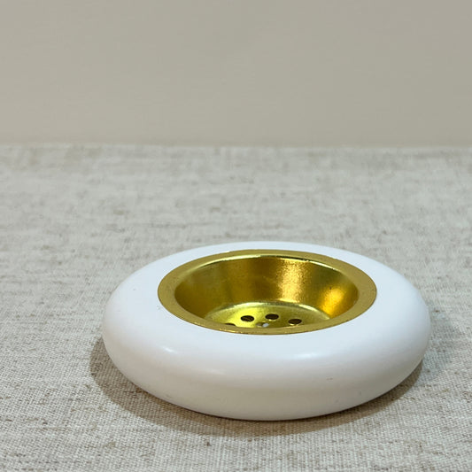 Round low white bukhoor burner with gold metal plate on a textured gray surface