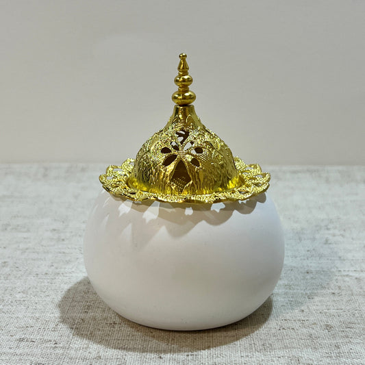 Sahar bukhoor burner with gold dome lid on a white round base against a textured gray background