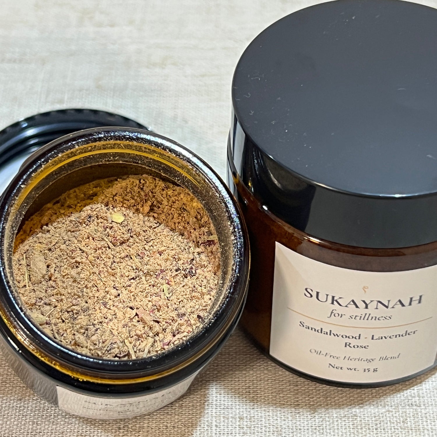 Open jar of oil-free bukhoor called Sukaynah from MINKO HOME on a textured fabric background